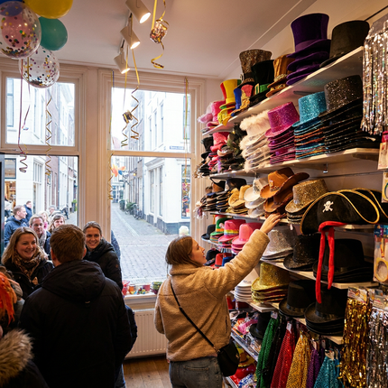 Kleurrijke carnaval hoeden liggen en hangen in een feestwinkel, met glitterhoeden, hoge hoeden en piratenhoeden in een vrolijke setting.